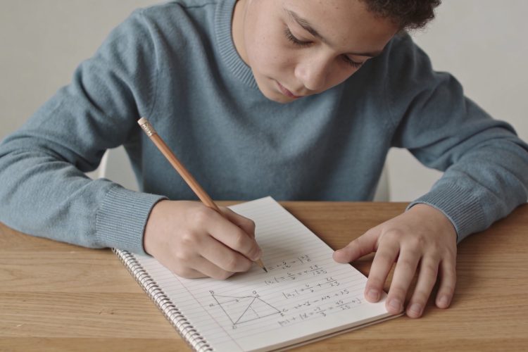 eleve assis resolvant exercice de math sur cahier