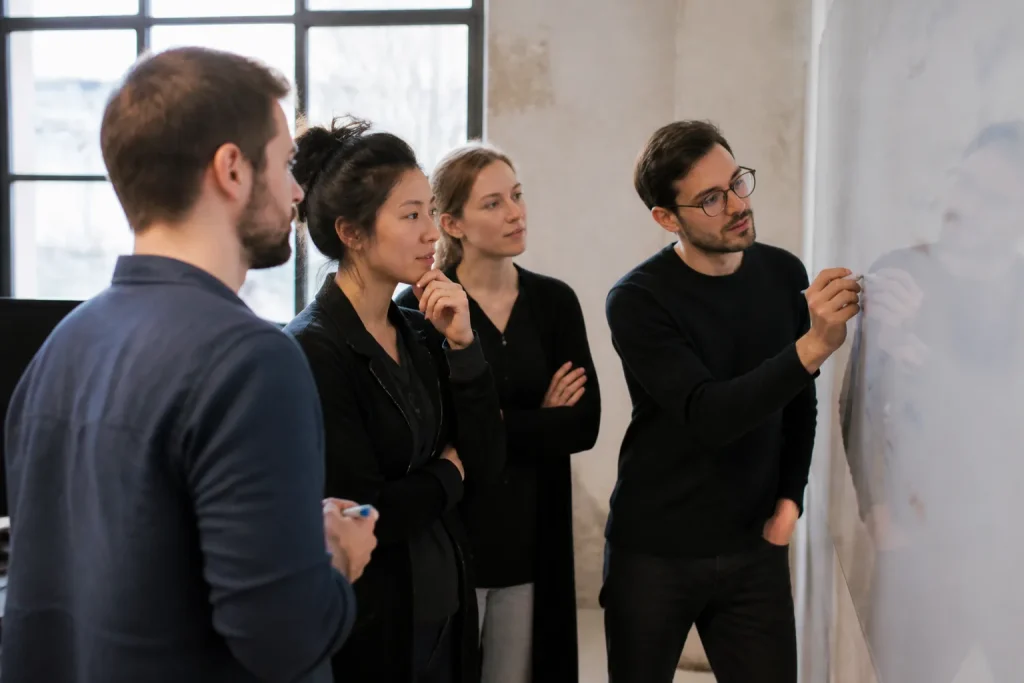 Quatre collegues analysent des notes sur un tableau blanc