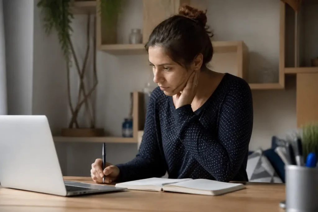 Femme devant ordinateur portable avec carnet et stylo
